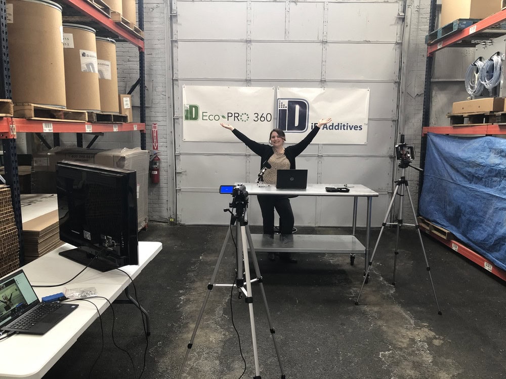 Woman presenting in a warehouse with iD Additives banners and equipment.