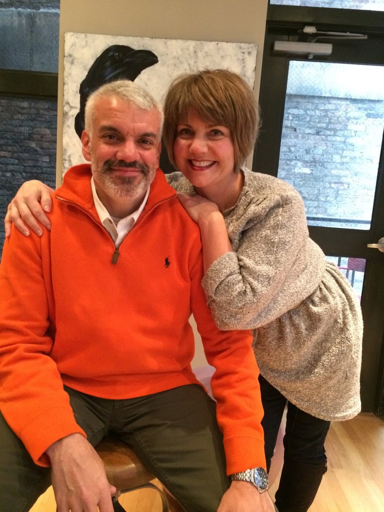 Two smiling people, a man and a woman, in a cozy indoor setting.