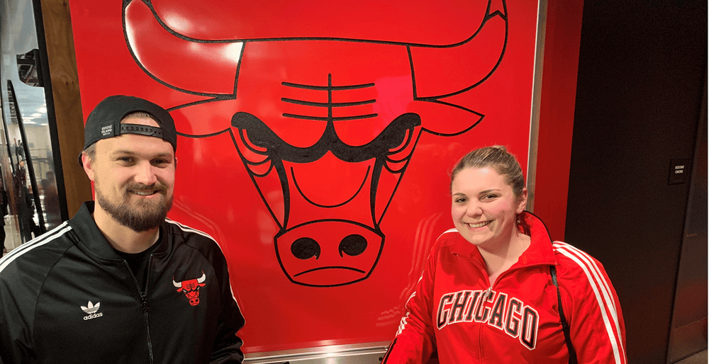 Two smiling people in Chicago sports apparel in front of a bull mural.