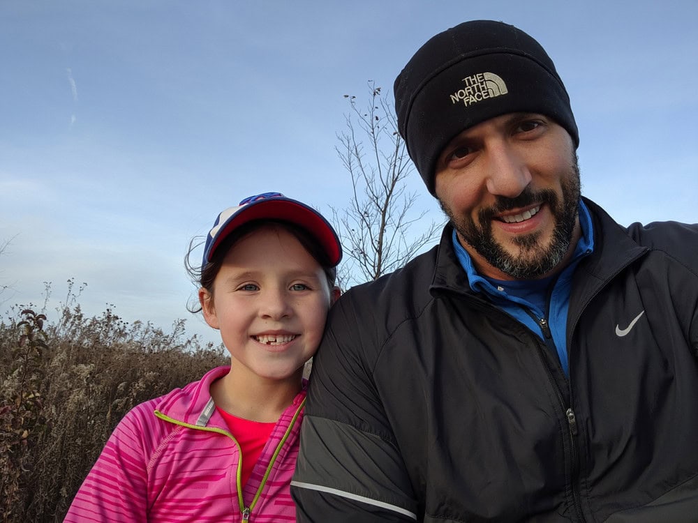 Man and girl smiling outdoors during a walk, wearing outdoor gear.