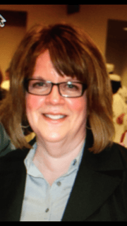 Smiling woman with glasses and shoulder-length brown hair at a professional event.